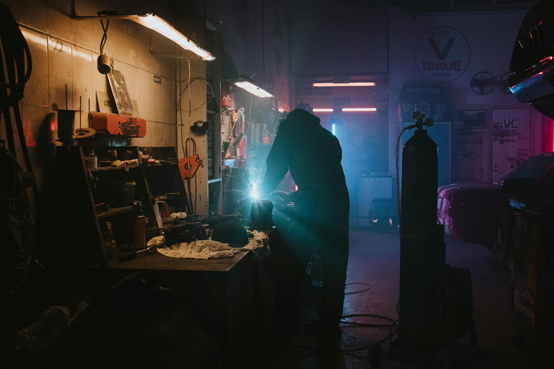 Mechanik spawający element auta w warsztacie oświetlonym neonami